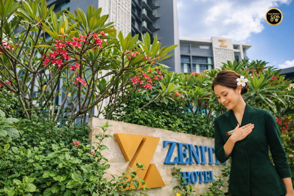 Spa therapist greeting guests at entrance of Zenith Hotel Putrajaya surrounded by lush greenery